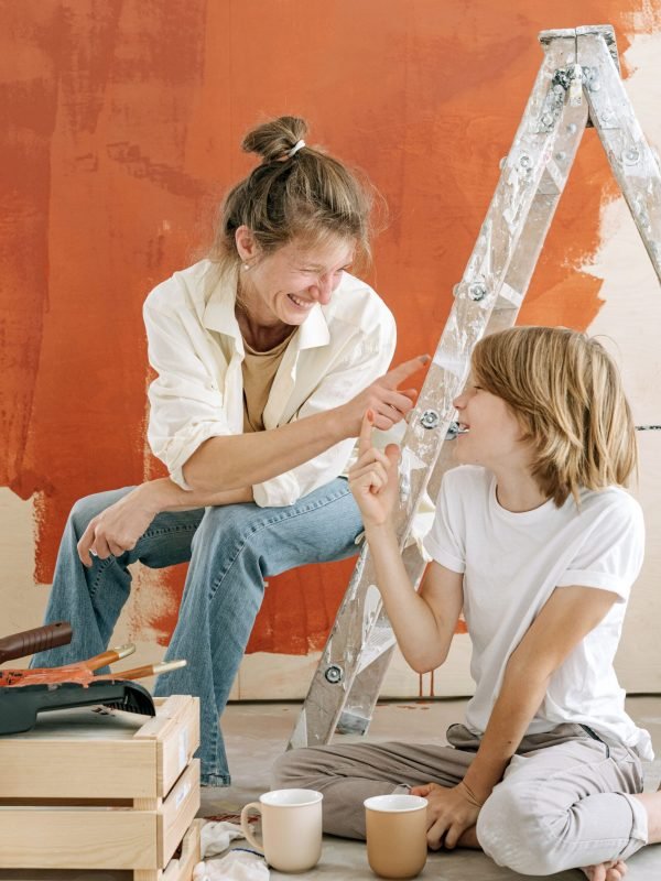 home-improvement-diy-painting-renovation Two people working on a DIY home improvement project with a ladder, tools, and an orange painted wall.